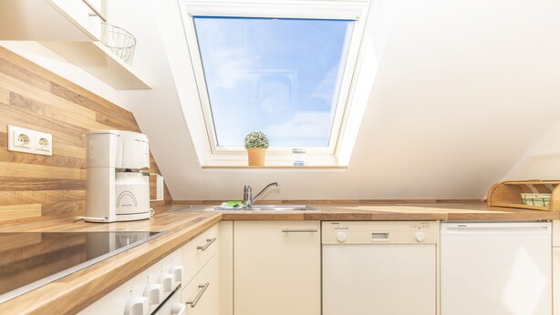 A modern kitchen with a skylight, wooden countertop, white appliances, and a small potted plant. - Apartment with sea views (Grömitz)