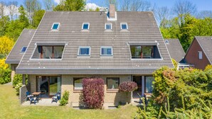 A modern two-story house with a sloped roof, large windows, and a small patio area with outdoor seating. - Apartment with sea views (Grömitz)