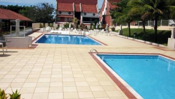 A swimming pool area with tiled flooring, lounge chairs, and umbrellas. - Village dos Pássaros (Guarapari)