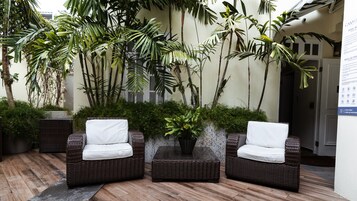Un área de estar al aire libre con techo, mobiliario de mimbre y plantas en macetas.