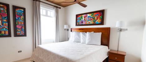 Une chambre à coucher avec un grand lit, un ventilateur de plafond, une table de chevet et deux lampes fixées au mur.