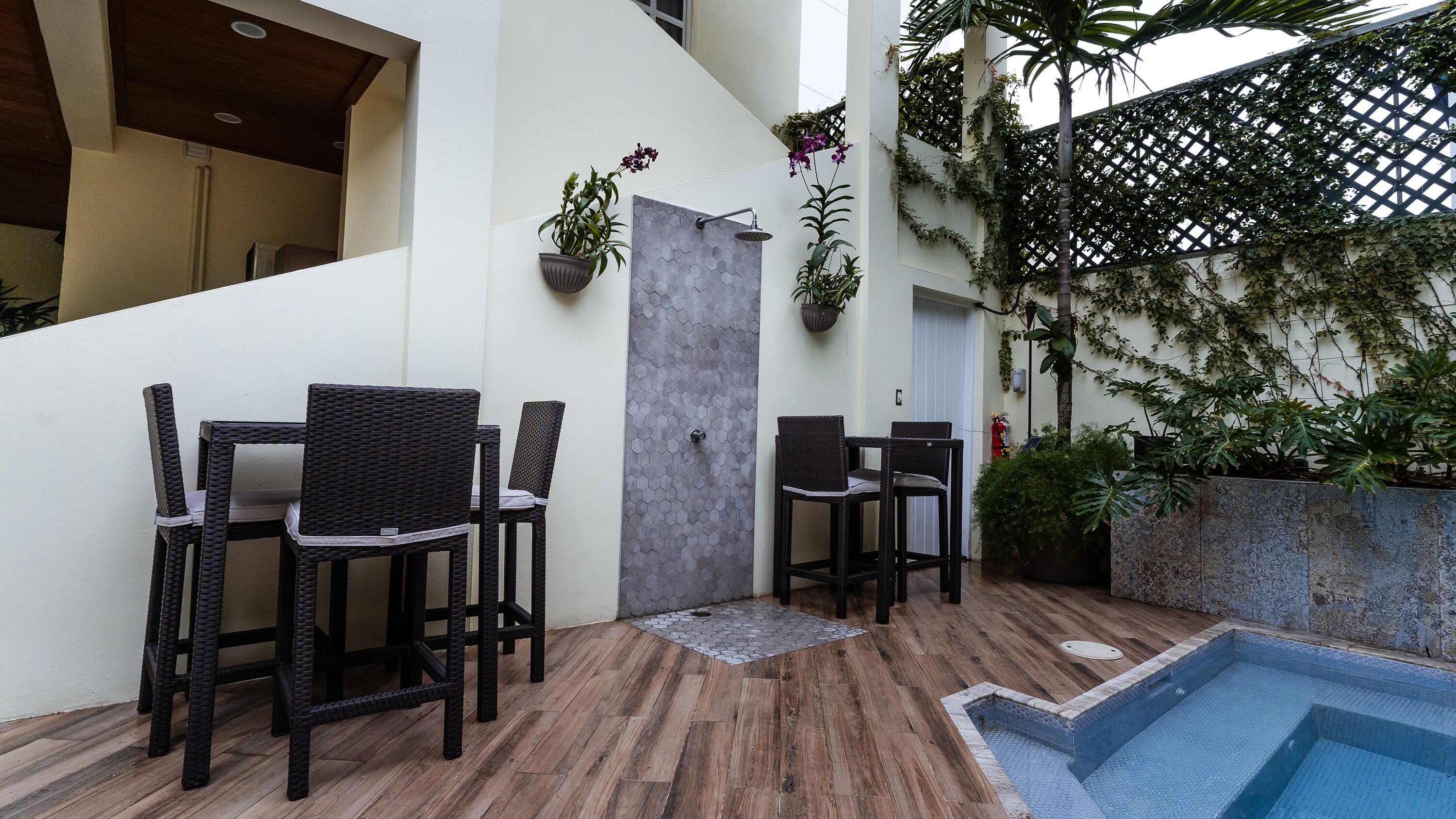 Un área de piscina con suelo de baldosas, una piscina pequeña y una zona de estar con sillas y una mesa.