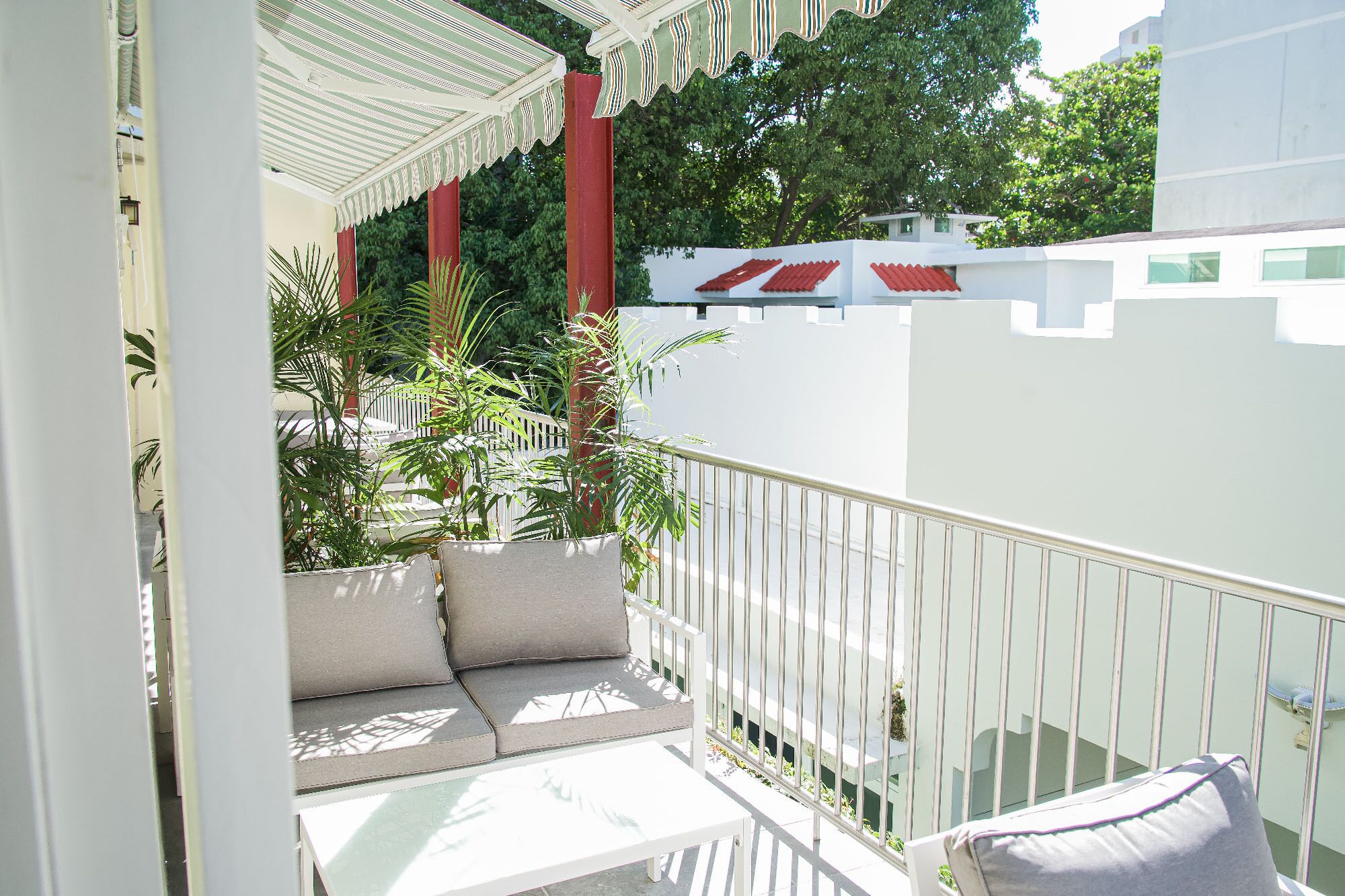 Un balcon doté d’une balustrade blanche, d’un espace salon avec des coussins et de plantes en pot.