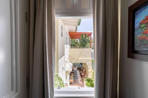 Vista a través de un umbral hacia un balcón con una pérgola de madera, mobiliario exterior y vistas a edificios y follaje.