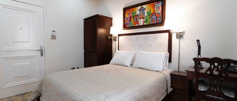 A bedroom with a bed, a desk, a chair, a wardrobe, and a painting on the wall.