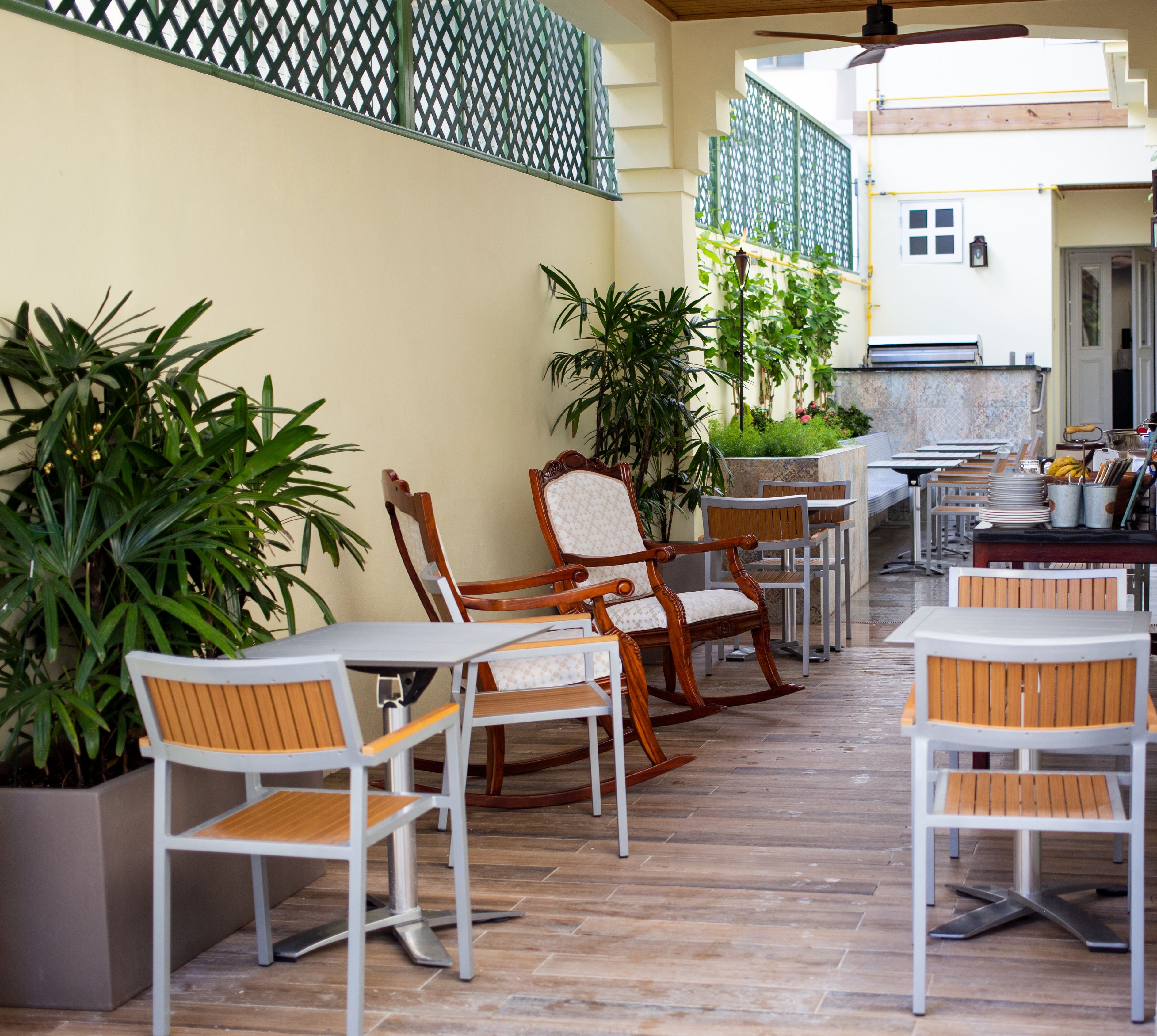 An outdoor patio with wooden and white chairs, tables, and potted plants.