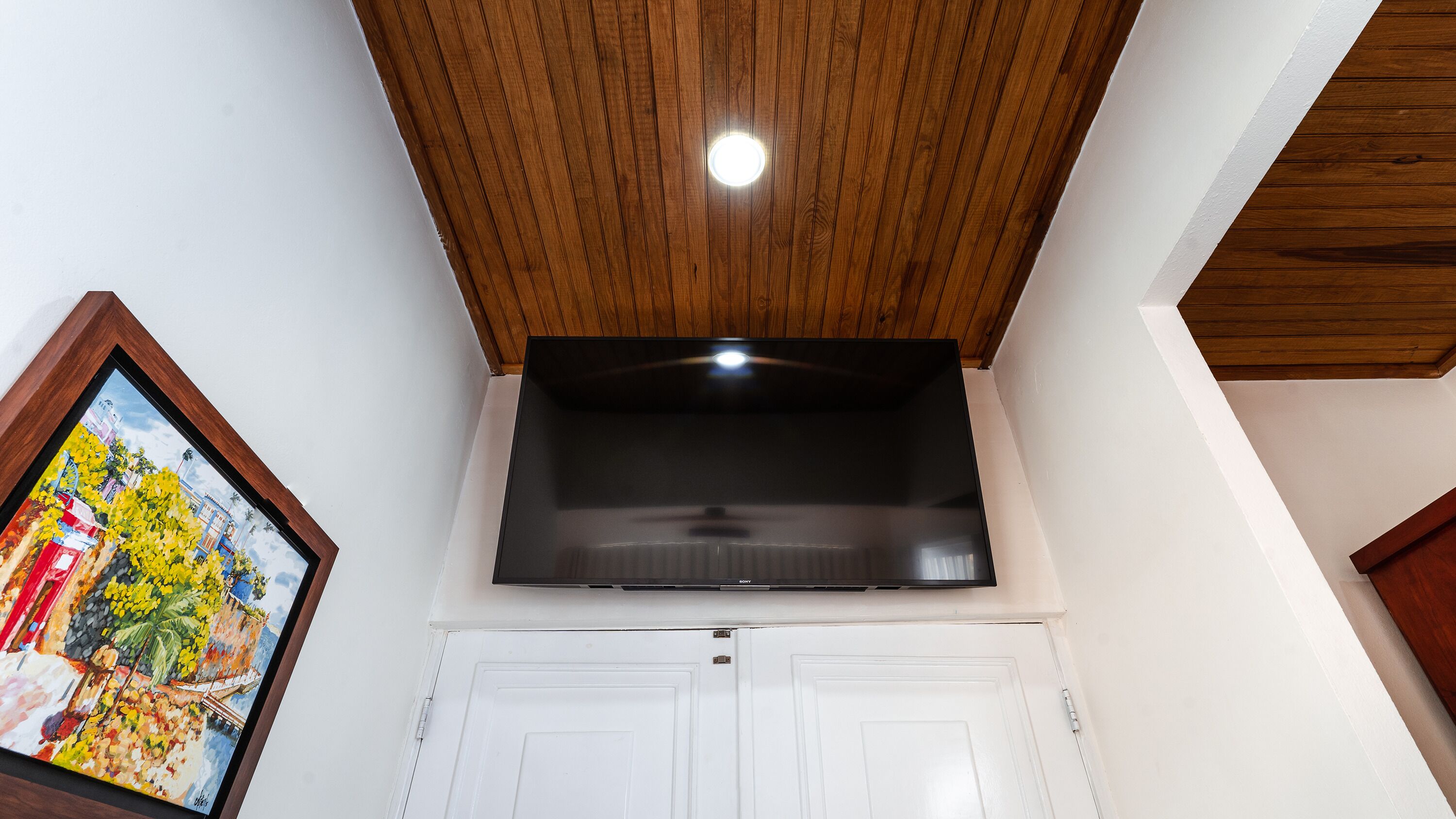 Ein Zimmer mit Holzbalkendecke, einem flachbildfernseher über einer weißen Tür und einem farbenfrohen Gemälde an der Wand.