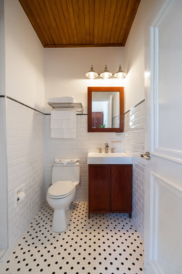 A small bathroom with white subway tiles, a wooden ceiling, a toilet, a sink, and a mirror. - Casa Wilson Inn (San Juan)