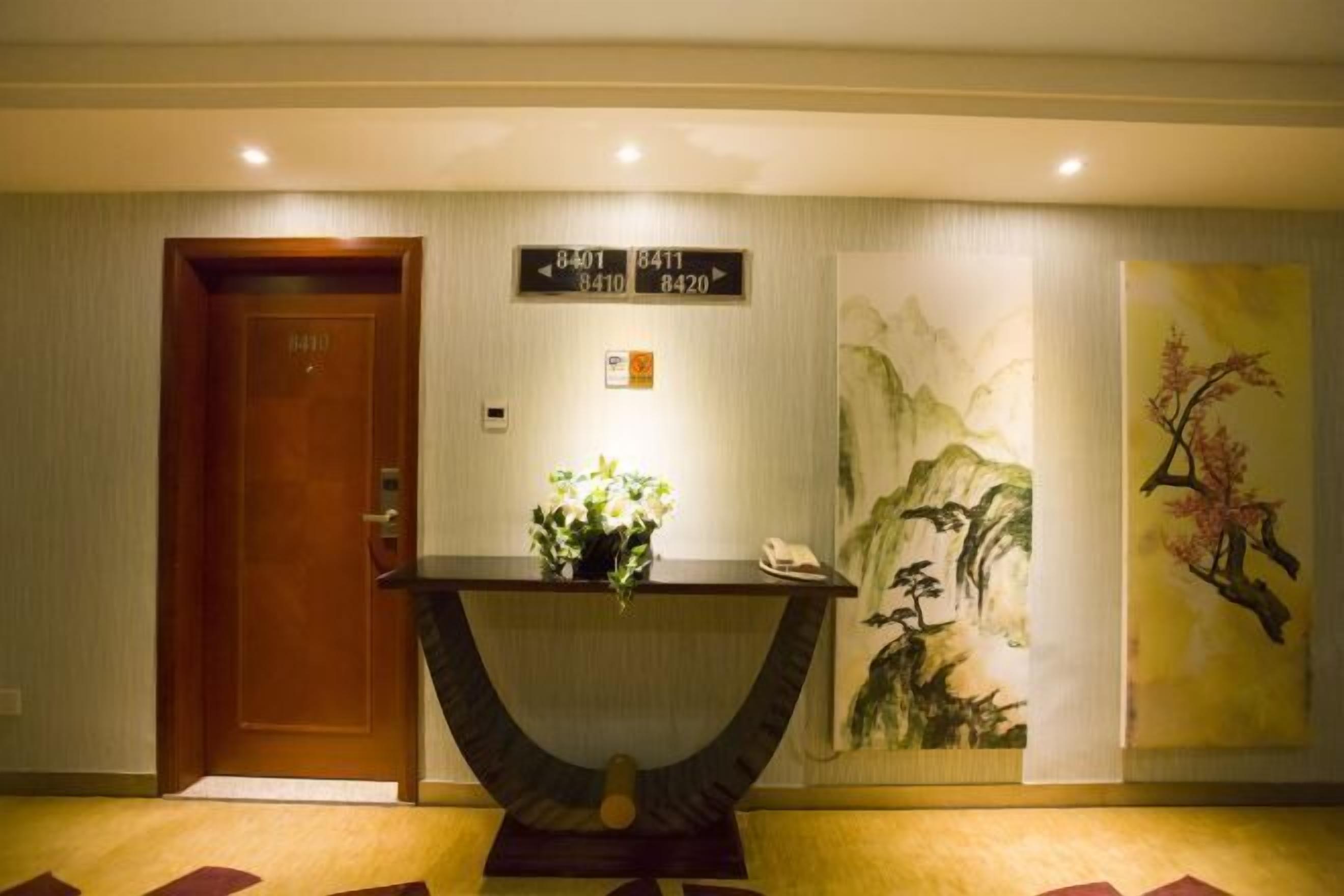 Un vestíbulo de hotel con una puerta de madera, una recepción con un florero y una pared con un cuadro.