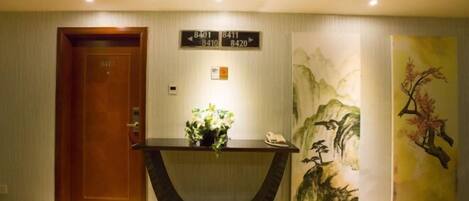 Un vestíbulo de hotel con una puerta de madera, una recepción con un florero y una pared con un cuadro.