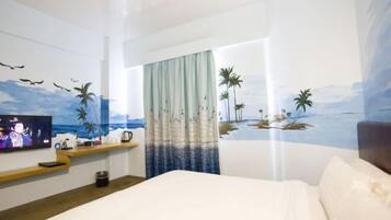 A hotel room with a bed, a TV on the wall, a shelf with items, and a mural of a beach scene.