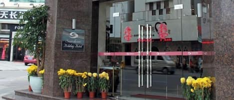 A hotel entrance with a red carpet, potted yellow flowers, and a sign for "Sunshine Holiday Hotel".