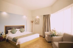 A hotel room with a bed, a nightstand, a chair, a desk, and a window with curtains. - Sunshine Holiday Hotel (Zhaoqing)