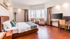 Ein Hotelzimmer mit einem Bett, zwei Sesseln, einem Schreibtisch, einem Fernseher und einem großen Fenster mit Vorhängen.
