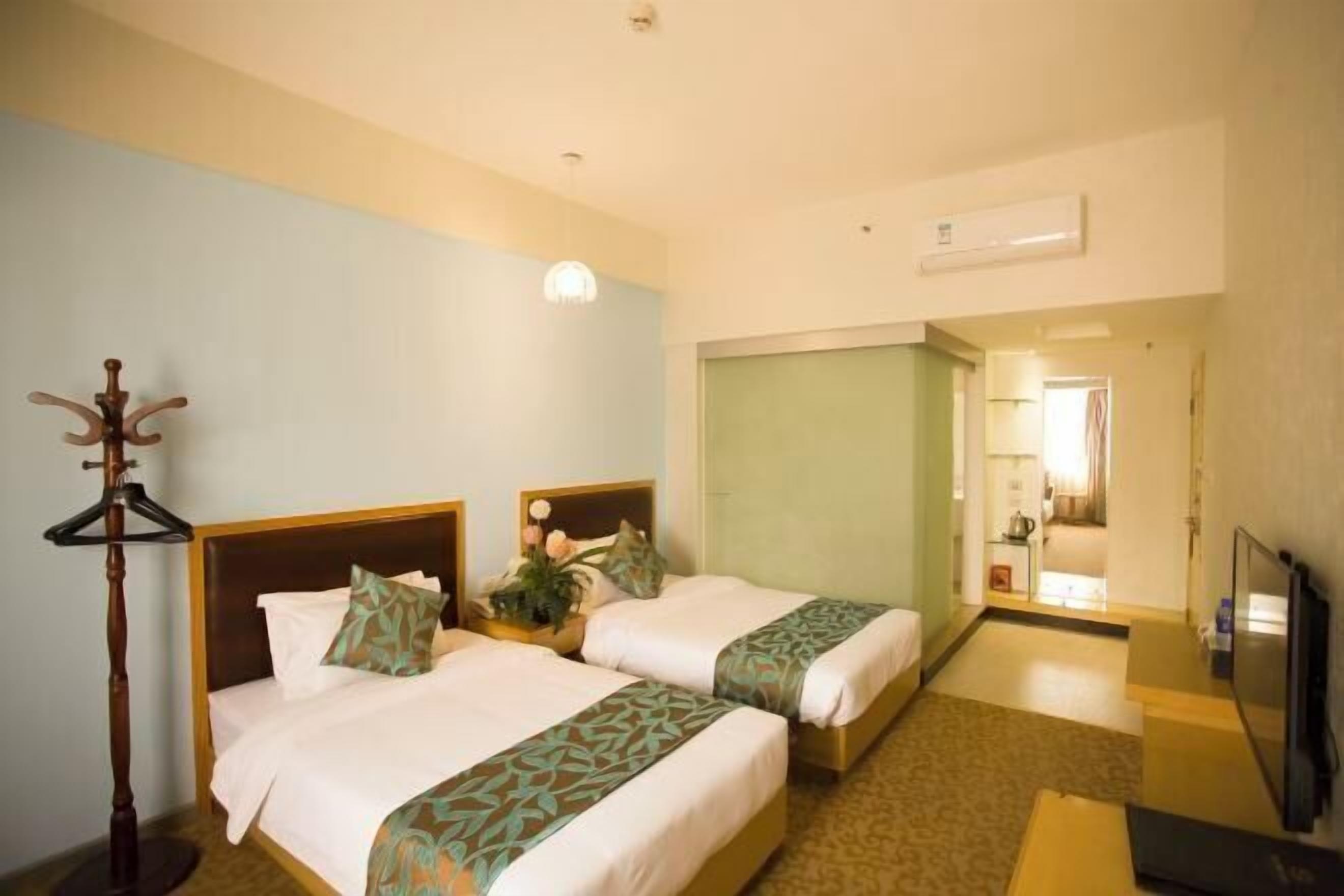 A hotel room with two beds, a wooden coat stand, a television, and a bathroom visible through an open door.