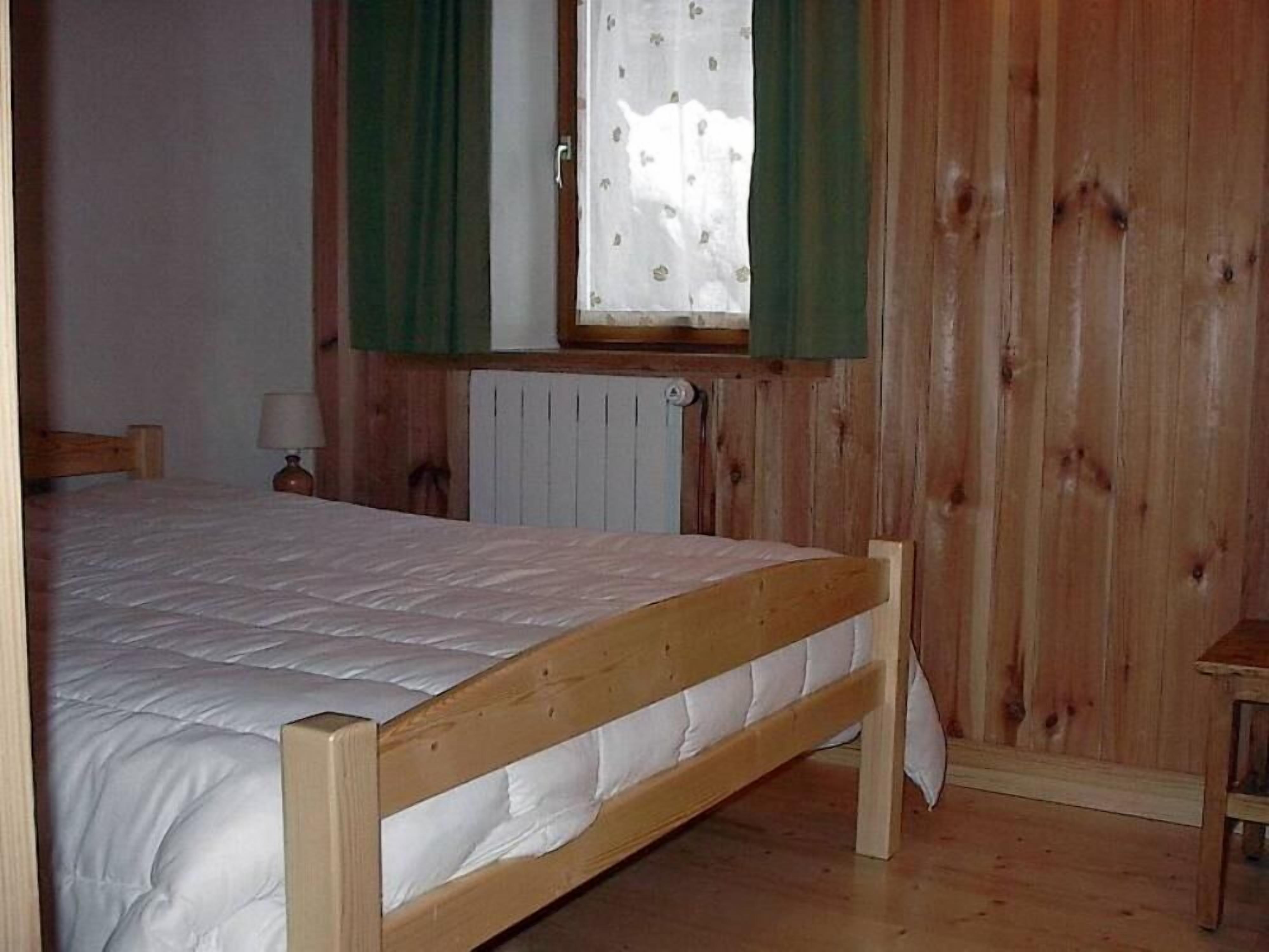 Ein Schlafzimmer mit Holzwänden, einem Einzelbett, einem Heizkörper und einem Fenster mit grünen Vorhängen.