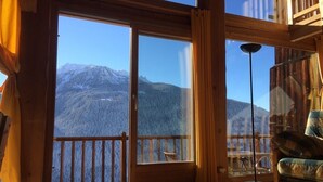 Une pièce dotée d’une grande porte-fenêtre coulissante donnant sur un balcon avec vue sur les montagnes.