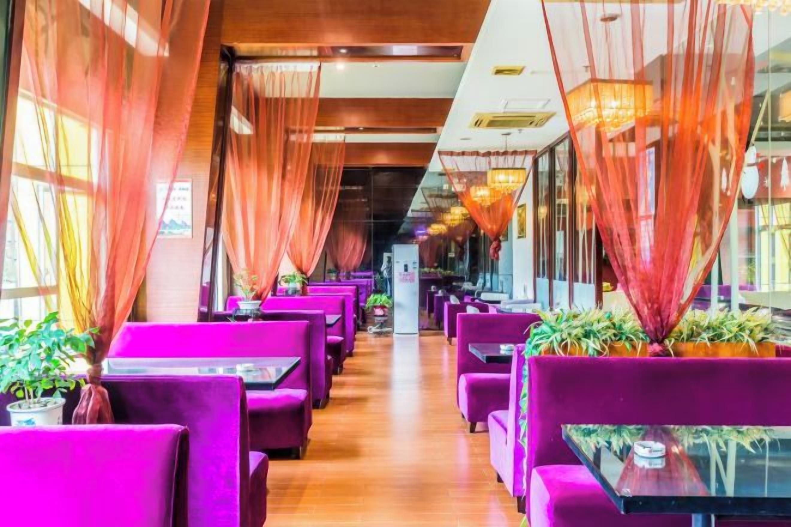 Un restaurante con filas de asientos morados, suelo de madera y ventanas amplias con cortinas.