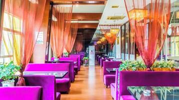 Un restaurante con filas de asientos morados, suelo de madera y ventanas amplias con cortinas.