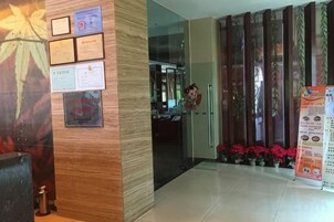 Zona de recepción con mostrador de madera, certificados enmarcados y puerta de vidrio que da a una cocina.