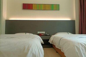 A hotel room with two single beds, a large headboard, a bedside table with a lamp, and a colorful abstract painting on the wall. - Ming Tien Inn (Fengkai)