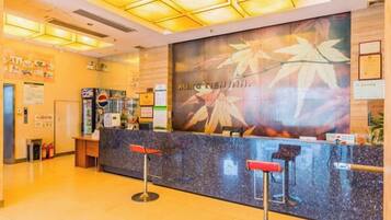 A reception area with a counter, two red bar stools, and a wall with a large poster.