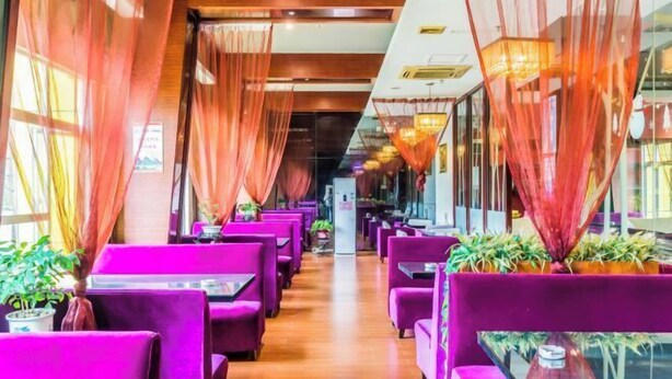 A restaurant with purple seating, large windows, and hanging lights.