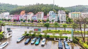A multi-story parking structure with cars parked inside, surrounded by greenery and buildings in the background.