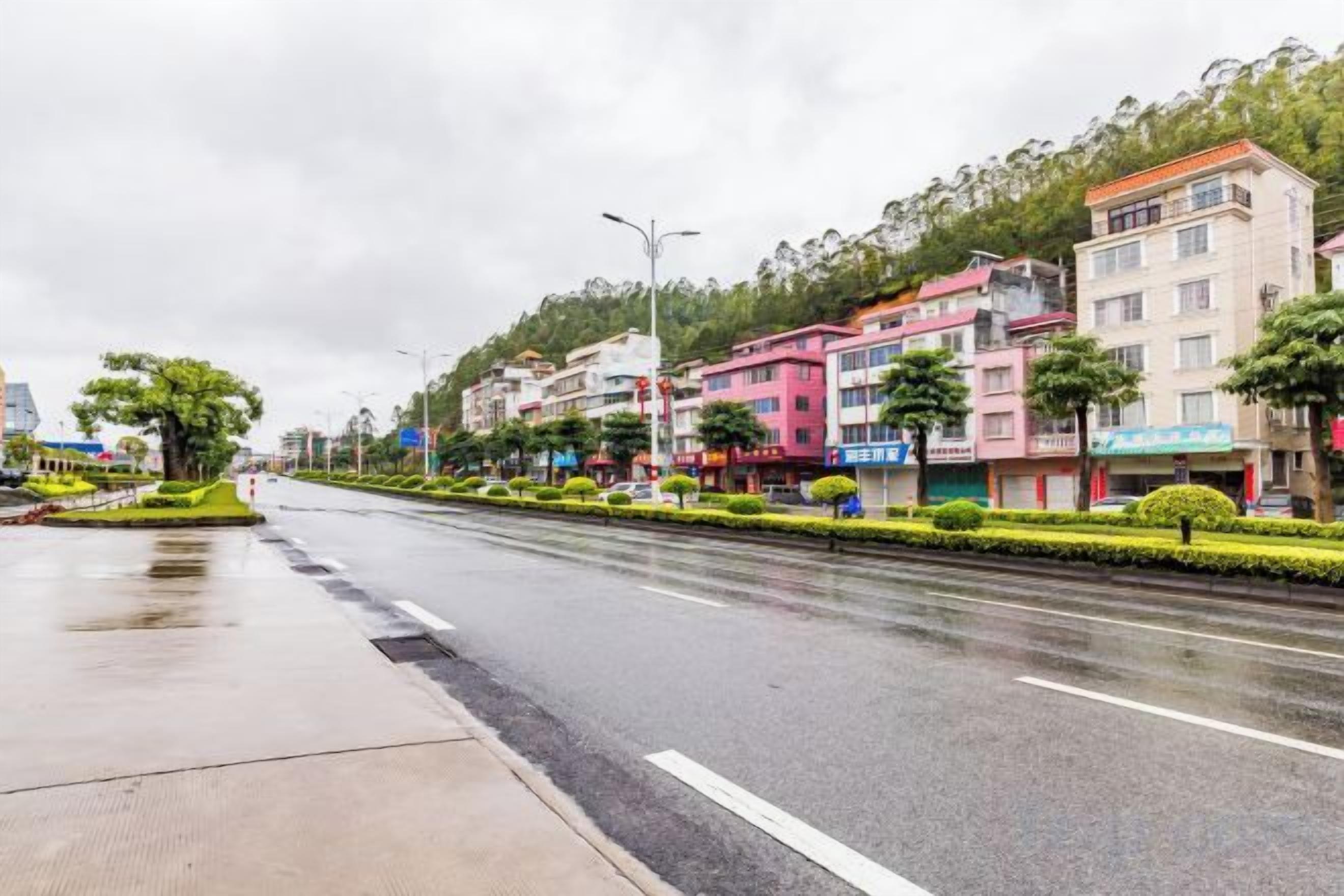 A multi-story building with a flat facade, a wide road with a median strip, and a wet surface indicating recent rain.