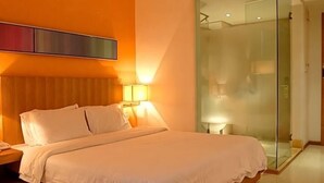 A hotel room with a bed, bedside lamps, a glass-enclosed shower, and a wall-mounted TV.