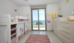 A child's room with bunk beds, a colorful rug, and a view of the sea through a glass door.