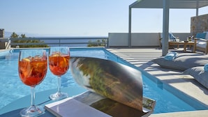 A poolside setting with two glasses of red drink, a menu, and a book on a table.