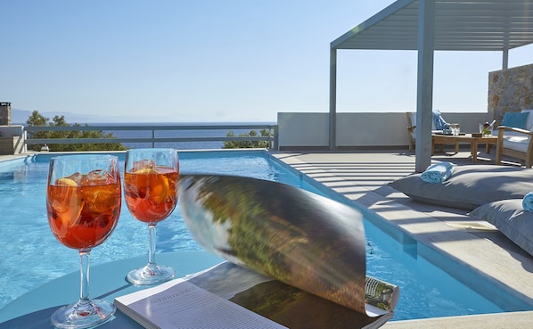 A poolside setting with two glasses of red drink, a menu, and a book on a table.