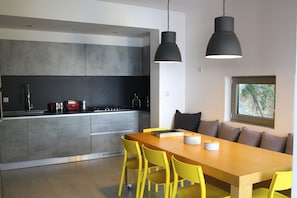 A modern kitchen with grey cabinets, a wooden dining table with yellow chairs, and two pendant lights.