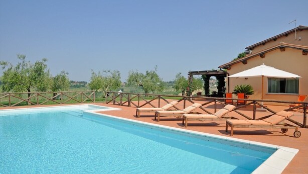 Ein Swimmingpool mit Liegestühlen und einer Pergola, umgeben von einem Holzzaun und viel Grün.
