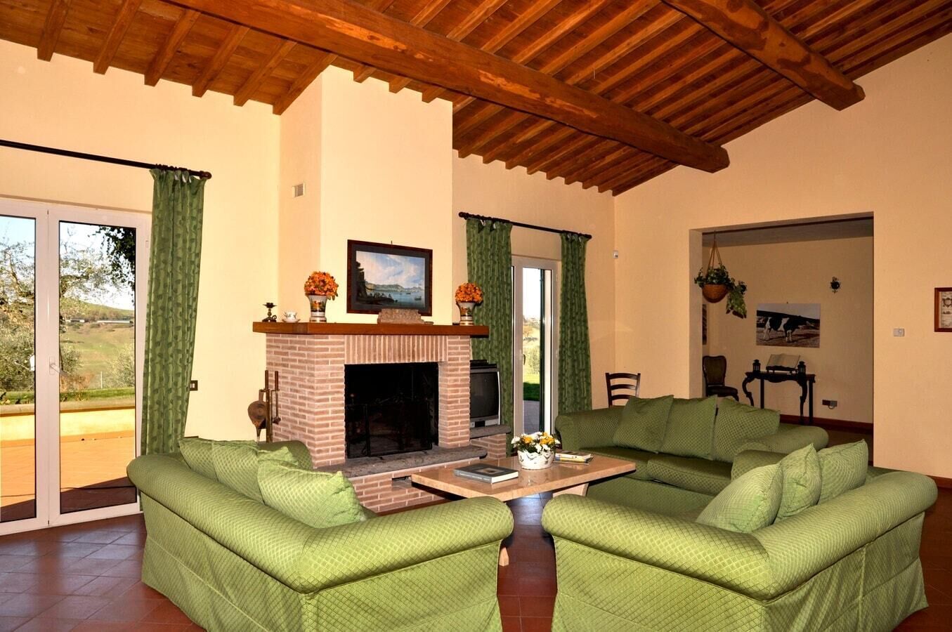 Un salón con chimenea, muebles tapizados en verde y vistas a través de puertas de cristal amplias.