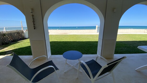 Une terrasse couverte avec vue sur la plage, comprenant deux chaises et une petite table.