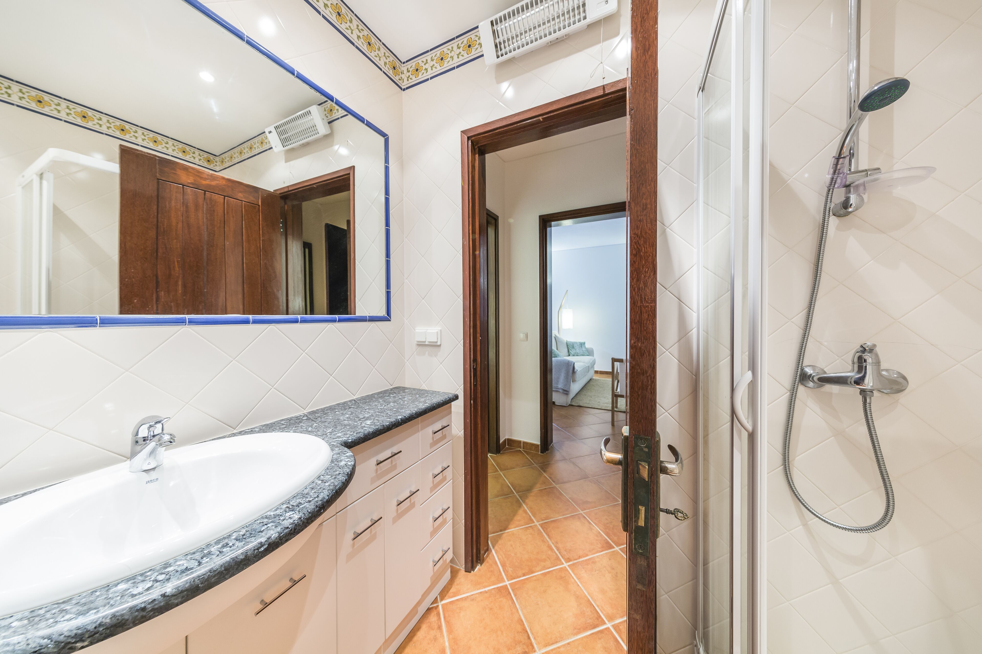 Un baño con lavamanos, espejo, ducha y suelo de baldosas.