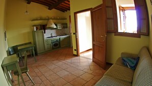 A kitchen with a stove, oven, and sink, a dining table with chairs, and a sofa in a living area with a window.