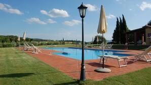 A swimming pool with lounge chairs and umbrellas, surrounded by a brick patio and greenery.