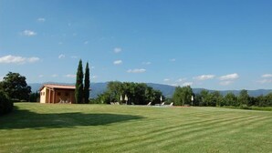 A grassy field with a building and trees in the background.