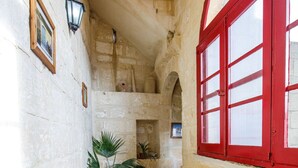 A narrow corridor with stone walls, a wooden bench, and a red-framed window. - Gozo, semi detached farmhouse with sunny terraces and free internet access. (Kercem)