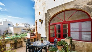 A courtyard with a round table and chairs, potted plants, and a red door. - Gozo, semi detached farmhouse with sunny terraces and free internet access. (Kercem)