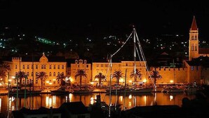 A historic building with a prominent tower, surrounded by palm trees and a waterfront. - New apartments  near the sea   (Seget Donji)