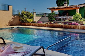 Una piscina con zona de descanso, una pérgola y un patio con mobiliario exterior.