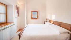 Une chambre d’hôtel avec un grand lit, une fenêtre avec des rideaux, un tableau encadré au mur et une petite table avec une lampe.