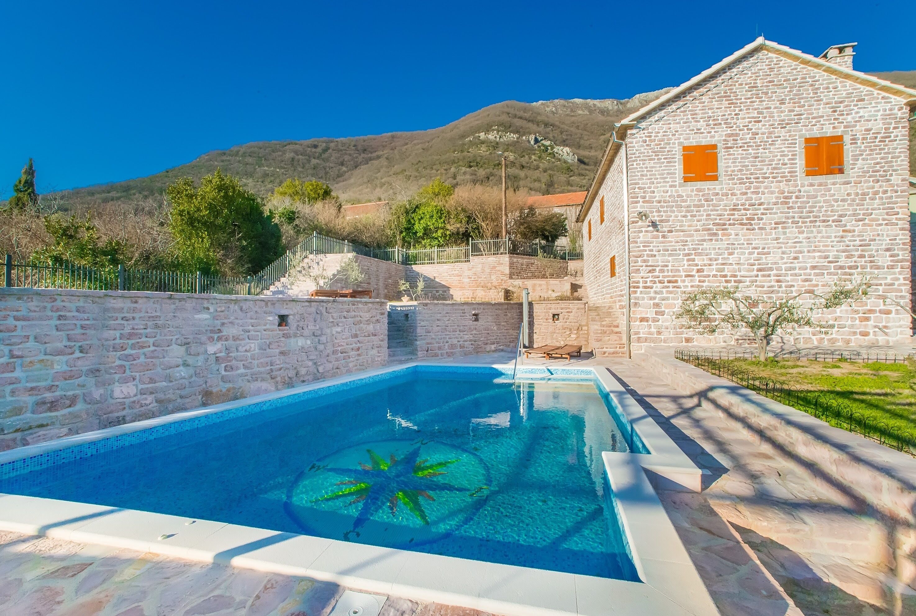 Una piscina con un adorno de estrella de mar, un edificio de piedra con contraventanas naranjas y montañas al fondo.