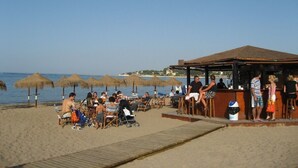 Un bar situé en bord de mer, avec des tables à l’extérieur et des parasols, offrant une vue sur l’océan.
