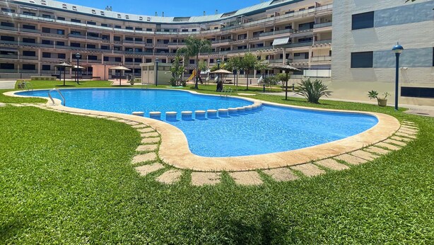 Une piscine entourée d’une pelouse bien entretenue, avec un immeuble à plusieurs étages en arrière-plan.
