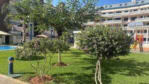 Une cour avec une piscine, plusieurs arbres et un espace de jeux pour enfants.